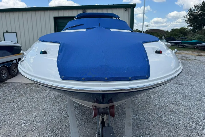 Slide: The Image of 2002 Sea Ray 240 Sundeck with blue cover, parked on gravel near storage facility. - 5