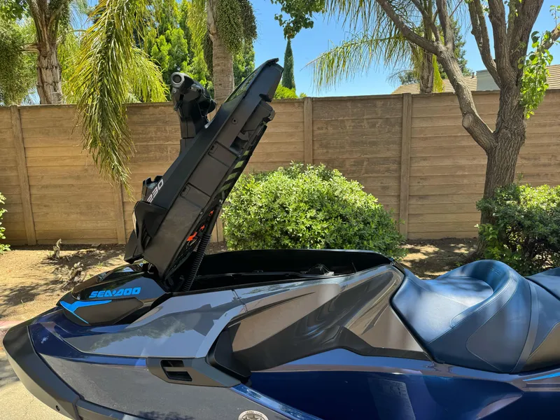 Slide: The Image of 2025 Sea-Doo GTX 230 with open storage compartment, parked near trees and a wooden fence. - 7