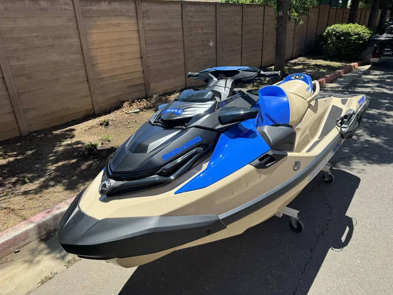 Slide: The Image of 2025 Sea-Doo Wake Pro 230 jet ski in blue and beige, parked outdoors. - 2