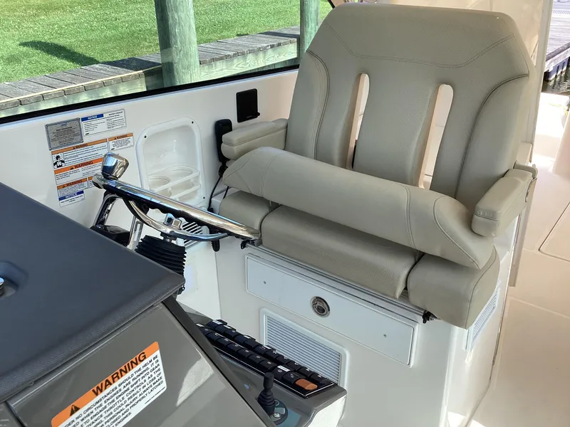 Slide: The Image of Captain's seat on 2017 Pursuit DC 325 Dual Console boat, featuring controls and warning labels. - 20