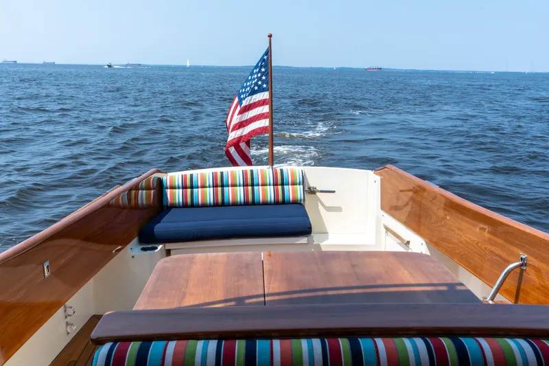 Slide: The Image of 2007 Hinckley Picnic Boat EP cruising with American flag, colorful seating, and wooden deck. - 19