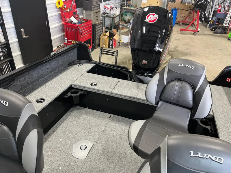 Slide: The Image of 2026 Lund 1800 Explorer Sport boat interior with seating and motor in a workshop. - 15