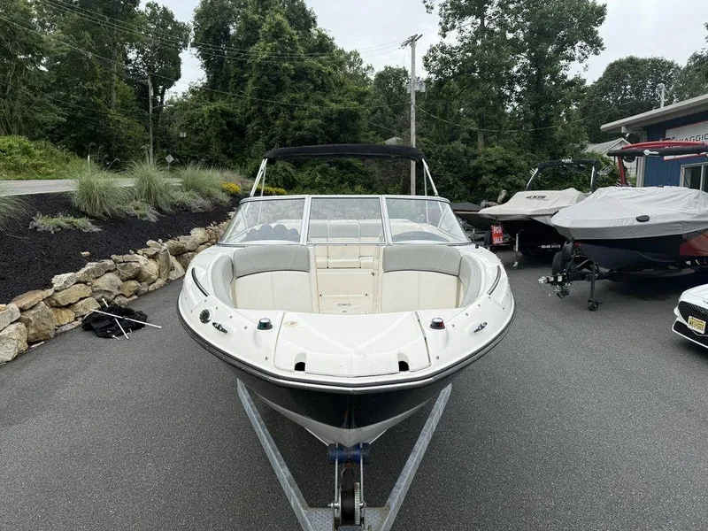 Slide: The Image of 2012 Bayliner 235 BR boat on trailer, parked outdoors with trees in background. - 2