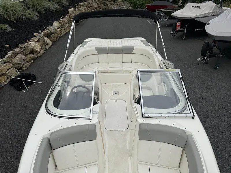 Slide: The Image of 2012 Bayliner 235 BR boat with open windshield, white and gray seating, parked on asphalt. - 3