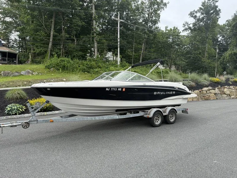 Slide: The Image of 2012 Bayliner 235 BR boat on trailer, parked on a road with lush greenery. - 7