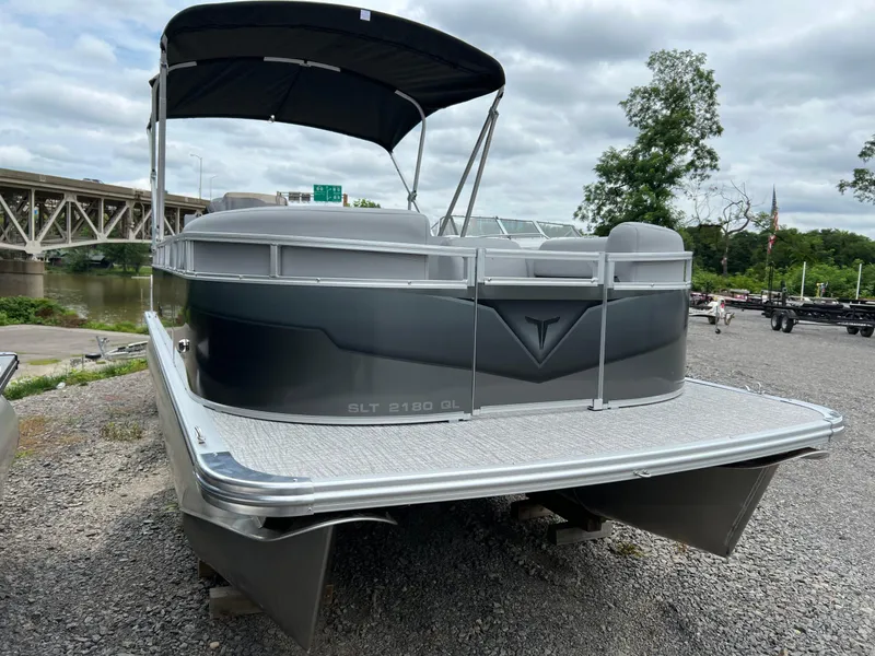 Slide: The Image of 2026 Tahoe Pontoon 2180 boat with canopy, parked on gravel near a river and bridge. - 3