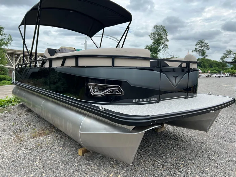 Slide: The Image of 2026 Tahoe Pontoon 2385 VRB, sleek black design, parked on gravel under cloudy sky. - 4
