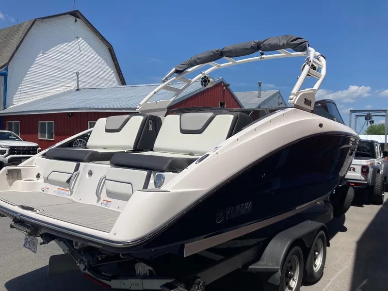 Slide: The Image of 2021 Yamaha Boats 252S on trailer, parked near rustic buildings under clear blue sky. - 10