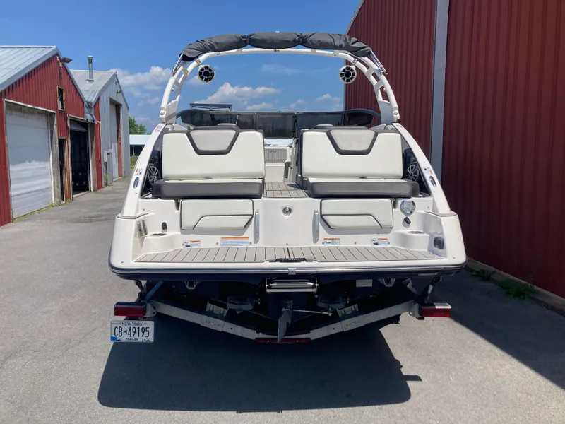Slide: The Image of 2021 Yamaha Boats 252S, rear view, parked near red building, showcasing seating and swim platform. - 9