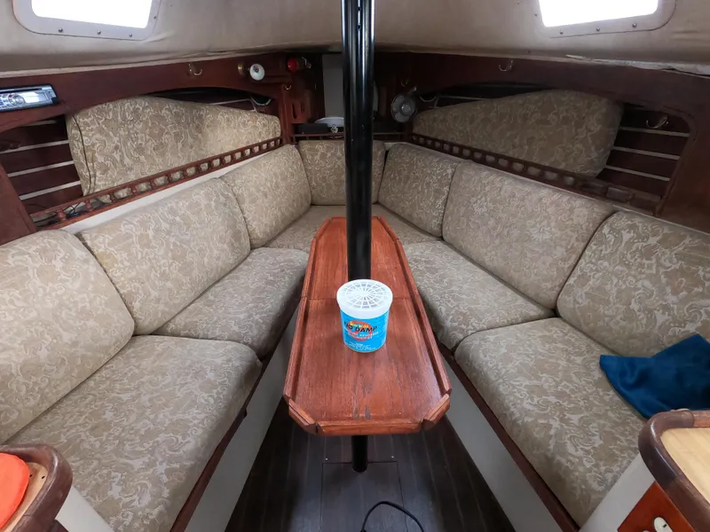 Slide: The Image of 1984 Lancer 30 sailboat interior with beige cushioned seating and wooden table. - 12