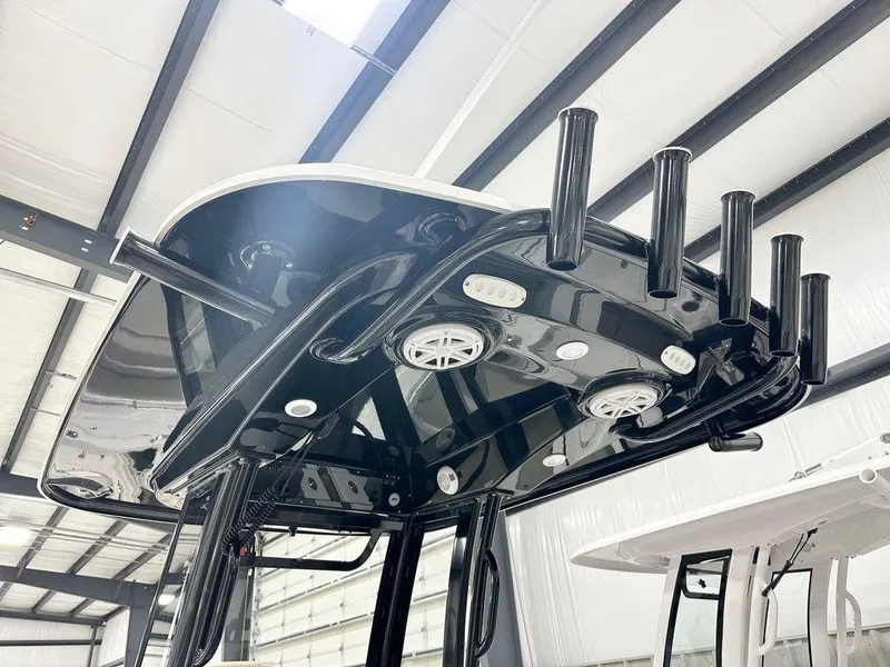 Slide: The Image of 2025 Sportsman Heritage 231 boat T-top with rod holders and speakers in a warehouse. - 3