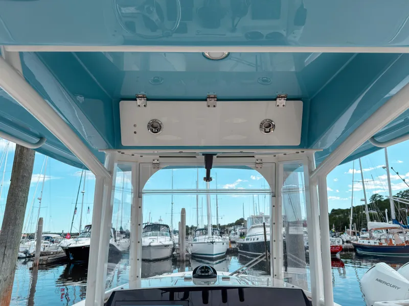 Slide: The Image of 2023 Cobia 280 Center Console boat interior view at marina, showcasing helm and overhead storage. - 40
