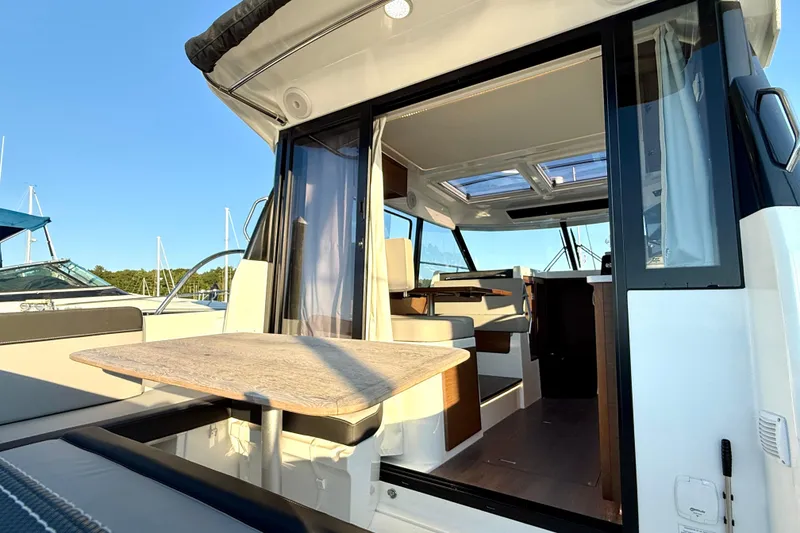 Slide: The Image of 2024 Jeanneau NC 1095 boat interior with seating and table, docked under clear blue sky. - 22