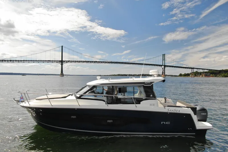 Slide: The Image of 2024 Jeanneau NC 1095 boat cruising near a bridge under a partly cloudy sky. - 6