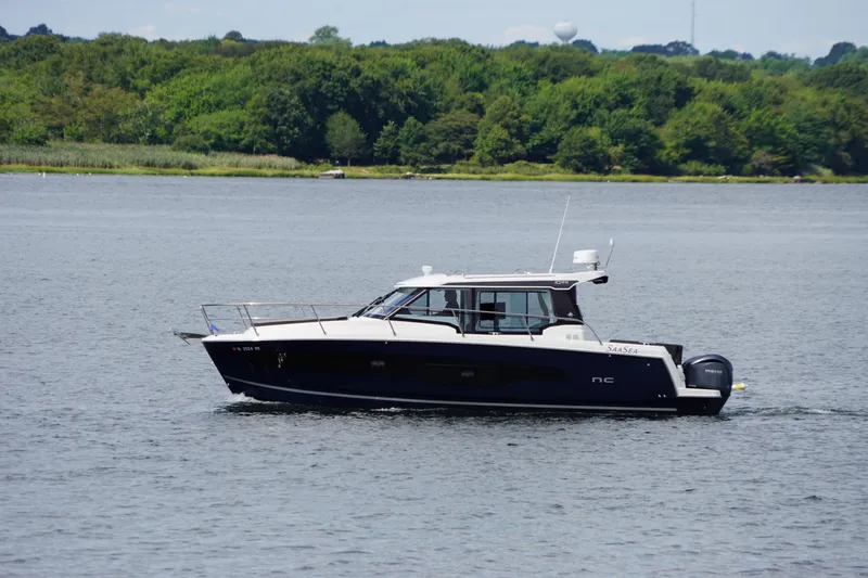 Slide: The Image of 2024 Jeanneau NC 1095 boat cruising on a serene lake with lush green background. - 7