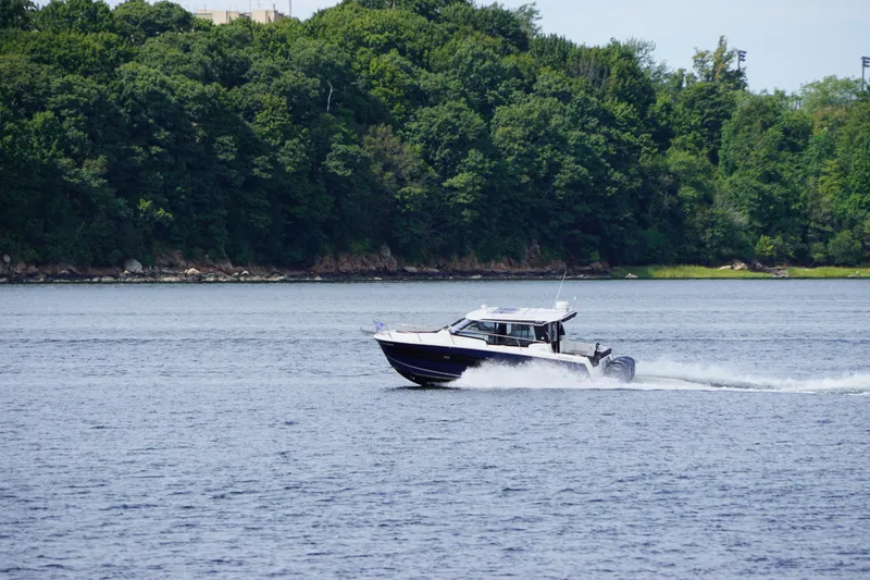 Slide: The Image of 2024 Jeanneau NC 1095 cruising on a serene lake with lush green forest backdrop. - 8