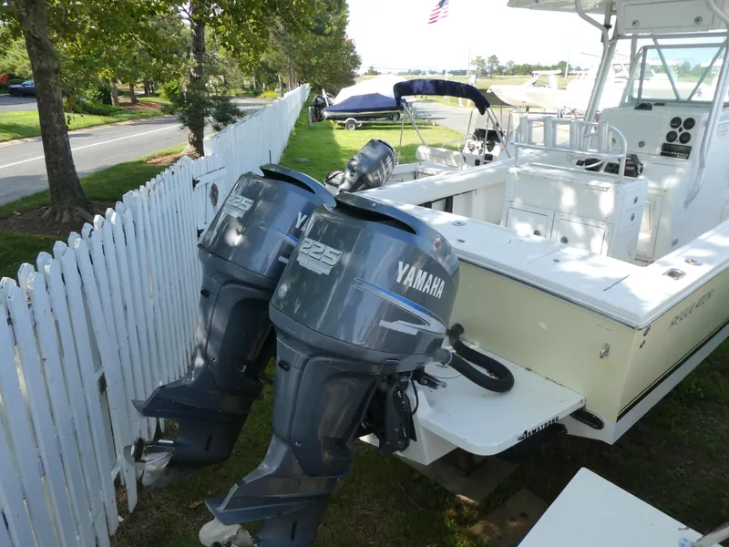 Slide: The Image of 2004 Regulator 26 Forward Seating boat with twin Yamaha 225 engines, parked near a white fence. - 4