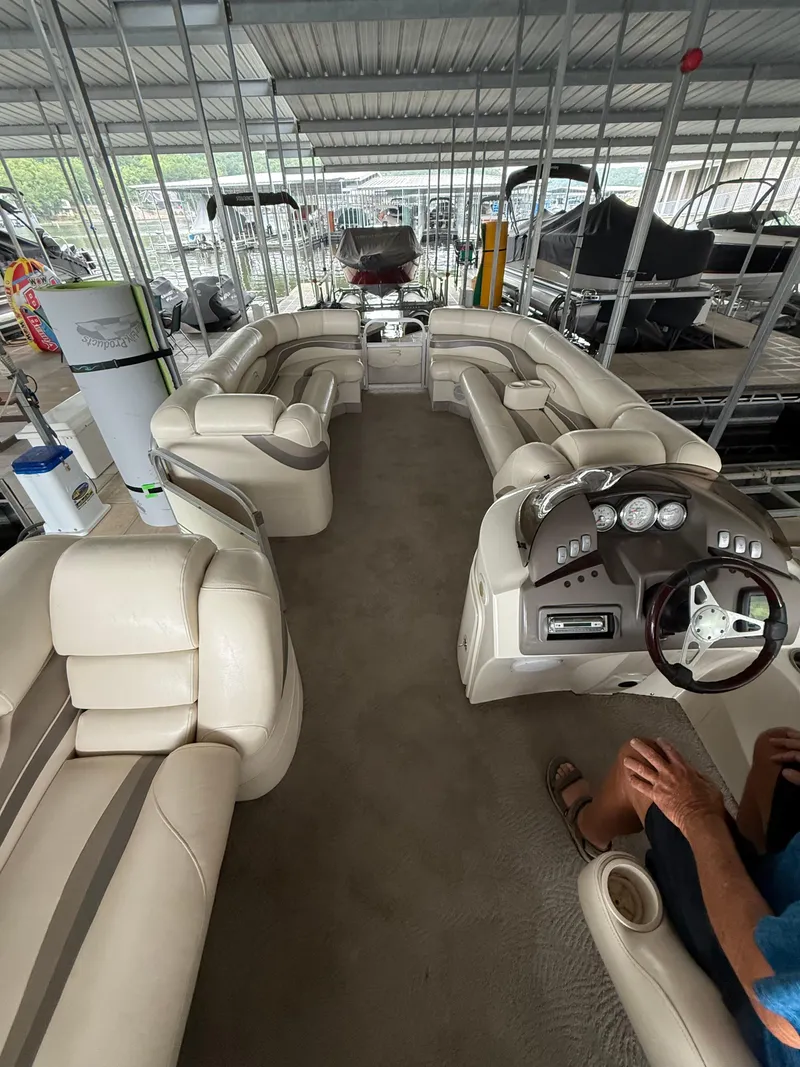 Slide: The Image of 2006 Bennington 2575RL I/O boat interior with beige seating and steering console in a covered dock. - 2