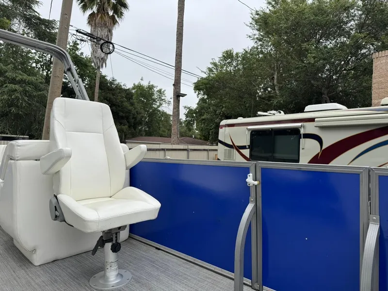 Slide: The Image of 2023 Frontier 24' Cruiser boat with white captain's chair and blue railing, parked near RV. - 10