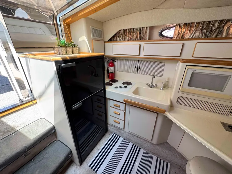Slide: The Image of Interior of 1995 Sea Ray 400 Express Cruiser with kitchenette, fridge, and striped rug. - 19