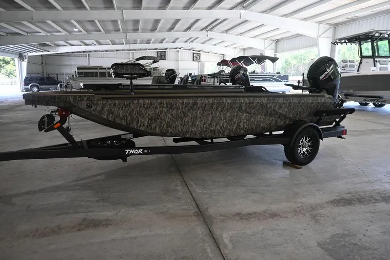The Image of 2026 Thor 1754 Timber Hammer boat in showroom, camo design, on trailer. - 1