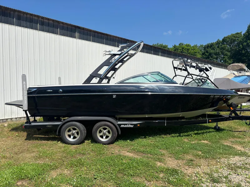 The Image of 2011 Malibu 21 vRide boat on trailer, parked outdoors near a building. - 0