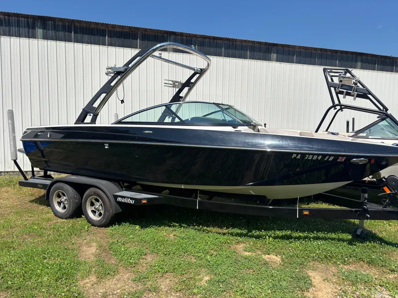 Slide: The Image of 2011 Malibu 21 vRide boat on trailer, parked outdoors near a metal building. - 3