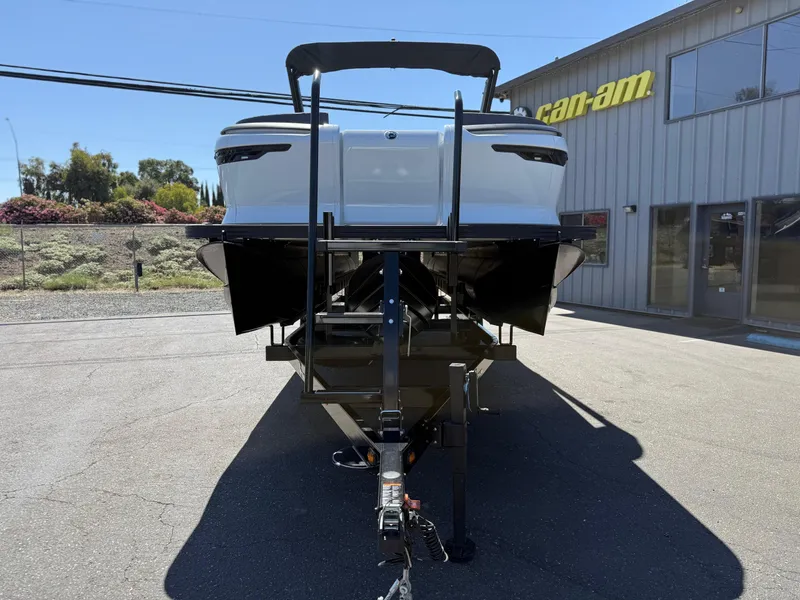 The Image of 2025 Manitou Explore Dual Engine boat on trailer outside dealership. - 1