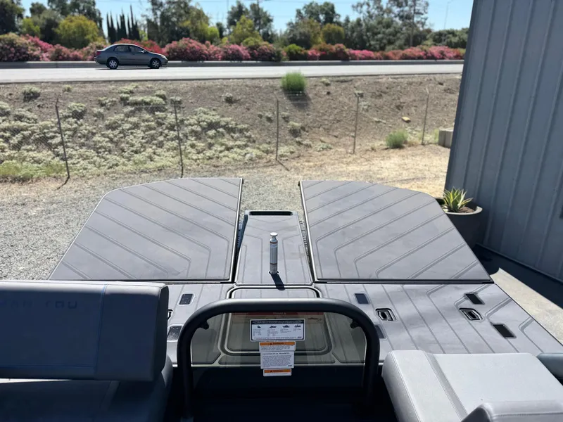 Slide: The Image of 2025 Manitou Explore Dual Engine boat with closed deck, parked near a road. - 16