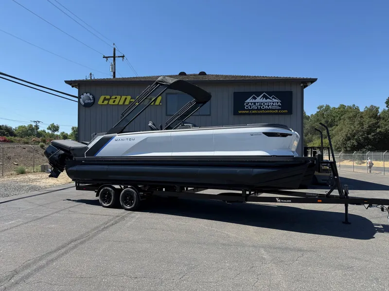 Slide: The Image of 2025 Manitou Explore Dual Engine boat on trailer outside California Custom shop. - 4