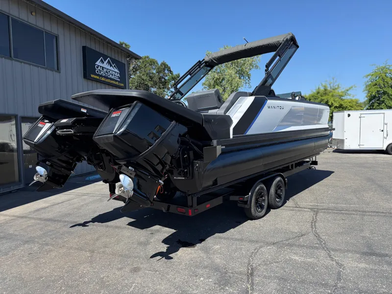 Slide: The Image of 2025 Manitou Explore Dual Engine boat on trailer, parked outdoors. - 6