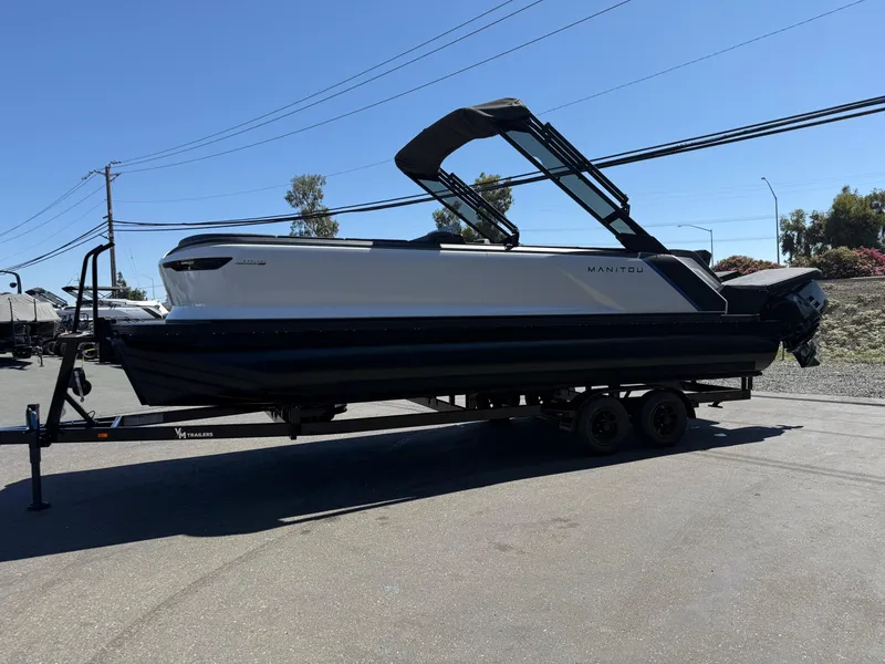 Slide: The Image of 2025 Manitou Explore Dual Engine boat on trailer under clear blue sky. - 8