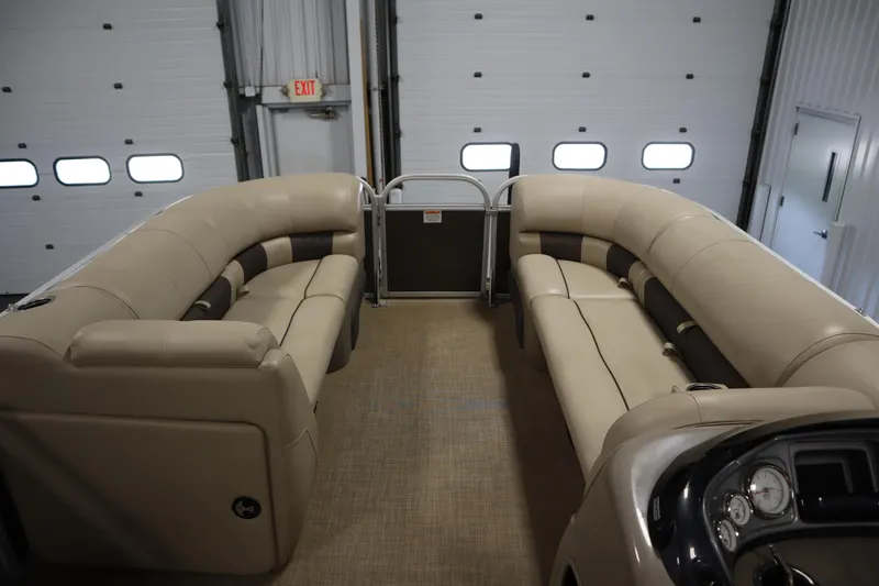 Slide: The Image of 2022 Tracker 20 Party Barge DLX interior with beige seating in a garage setting. - 11