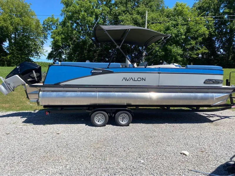 The Image of 2024 Avalon Catalina Entertainer pontoon boat on trailer, blue and silver design, parked outdoors. - 1