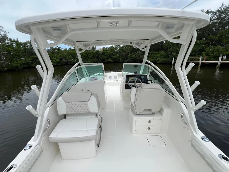 Slide: The Image of 2025 World Cat 230 DC boat interior with seating and helm, docked on calm water. - 19
