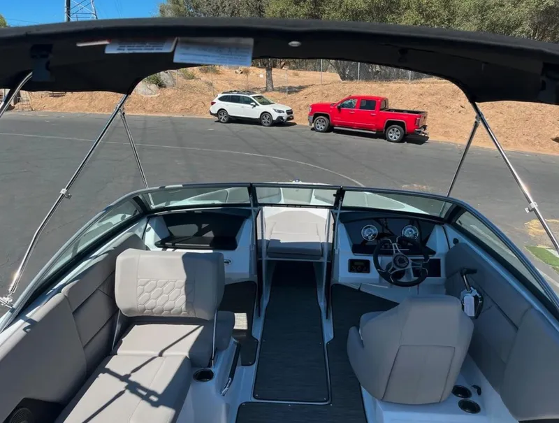 Slide: The Image of 2023 Four Winns H1 boat interior with seating and dashboard, parked near red and white vehicles. - 8