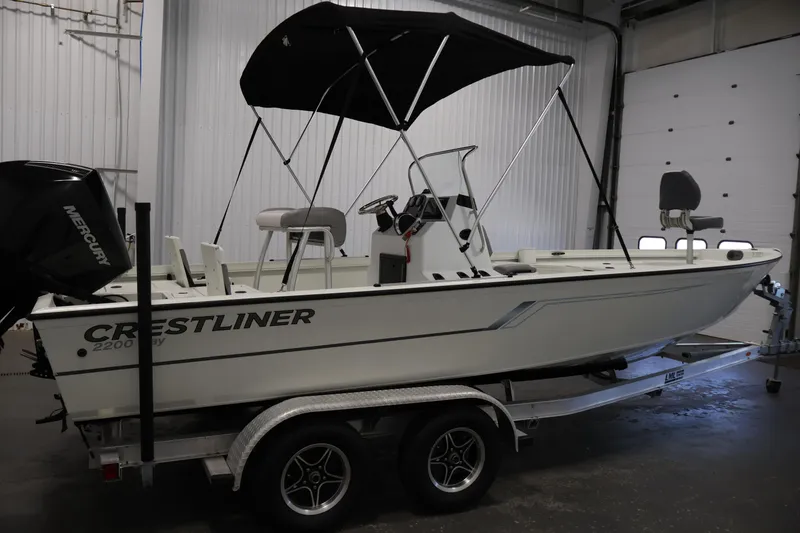 Slide: The Image of 2022 Crestliner 2200 Bay boat on trailer in indoor storage, featuring a Mercury engine. - 5