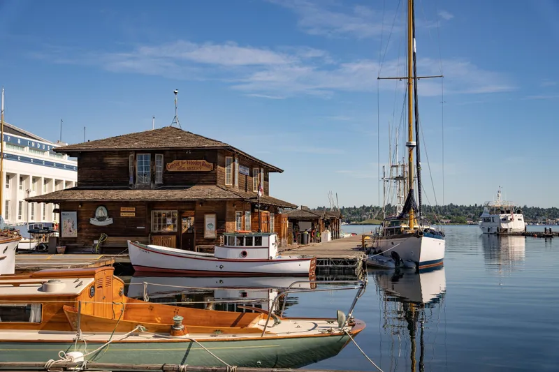 Slide: The Image of Wooden boathouse and sailboats at a serene marina under a clear blue sky. - 43