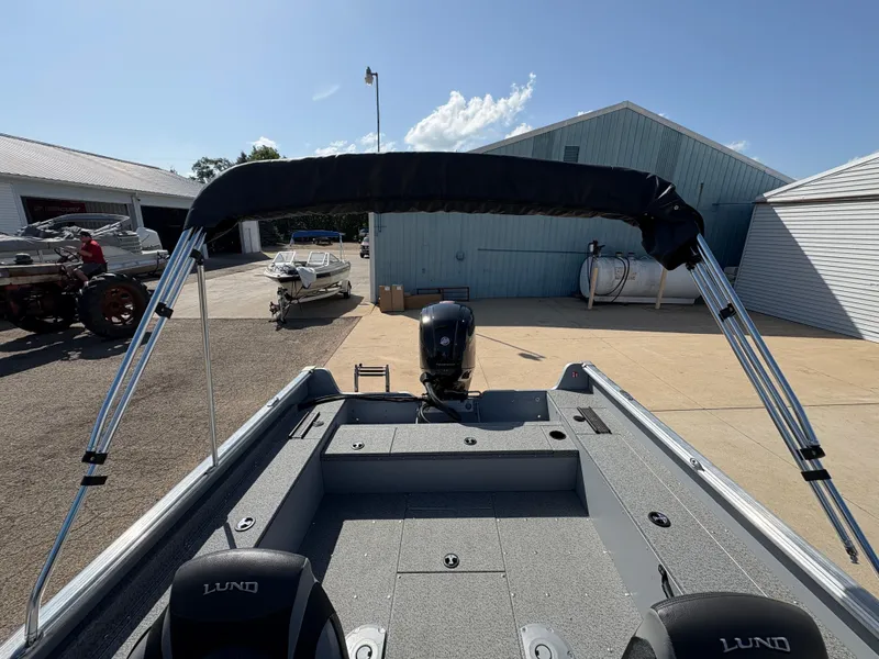Slide: The Image of 2025 Lund 1875 Alaskan Sport boat with canopy, parked outdoors under clear sky. - 14