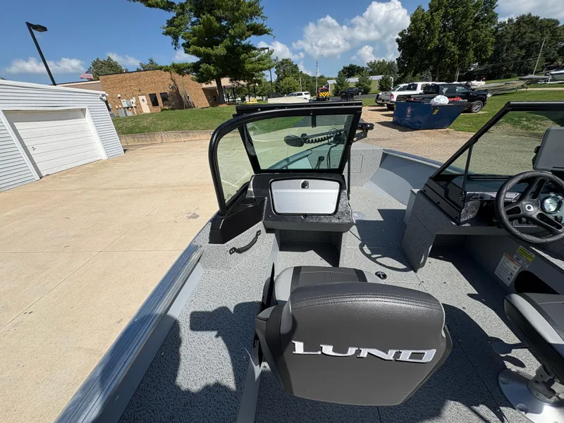 Slide: The Image of 2025 Lund 1875 Alaskan Sport boat interior with steering console and seating, parked outdoors. - 17