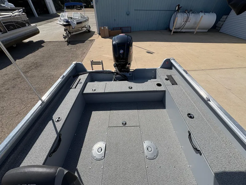 Slide: The Image of 2025 Lund 1875 Alaskan Sport boat interior with motor, docked outdoors. - 20