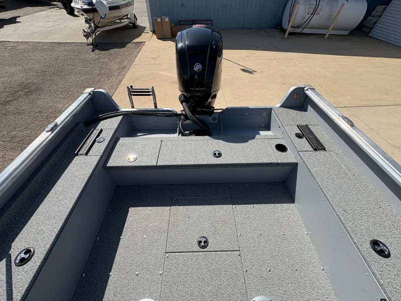 Slide: The Image of 2025 Lund 1875 Alaskan Sport boat interior with motor, gray flooring, and storage compartments. - 25