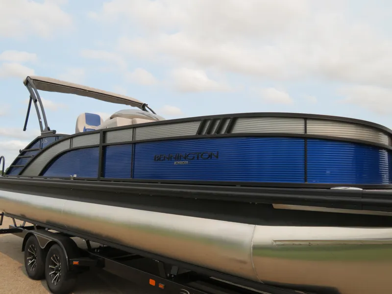 Slide: The Image of 2024 Bennington 25 LTSB pontoon boat on trailer, blue exterior, under cloudy sky. - 25