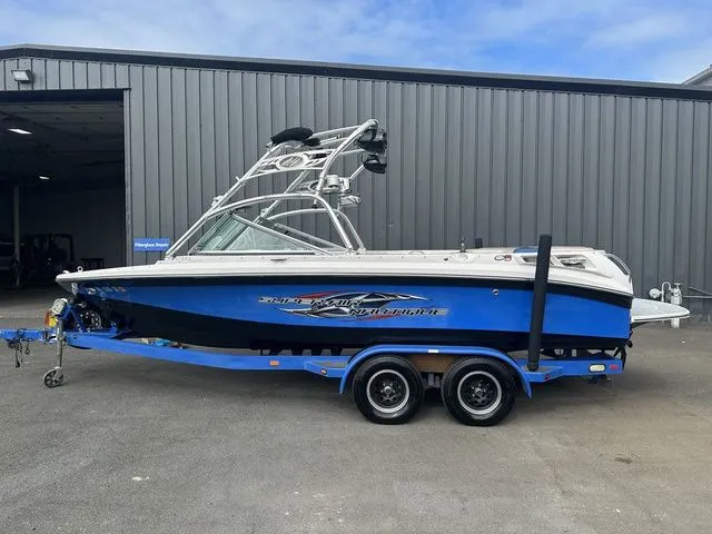 Slide: The Image of 2007 Nautique Super Air Nautique 210 boat on trailer, blue and white, parked outside a warehouse. - 1
