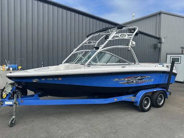 Slide: The Image of 2007 Nautique Super Air Nautique 210 boat on trailer, parked near a metal building. - 2