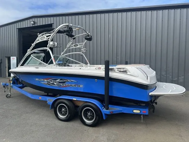 Slide: The Image of 2007 Nautique Super Air Nautique 210 boat on trailer, blue and white, parked outside a garage. - 4