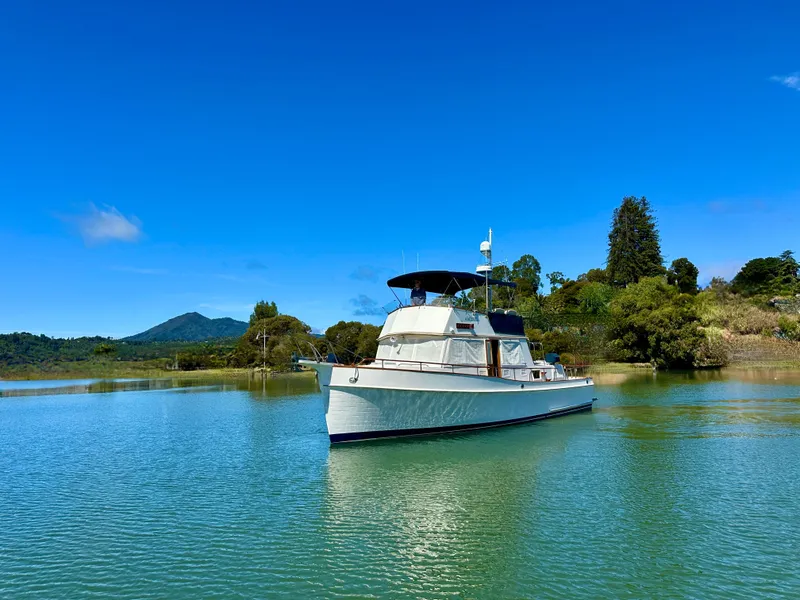 Slide: The Image of 1989 Grand Banks 42 Classic yacht on tranquil water with lush greenery and blue sky. - 3