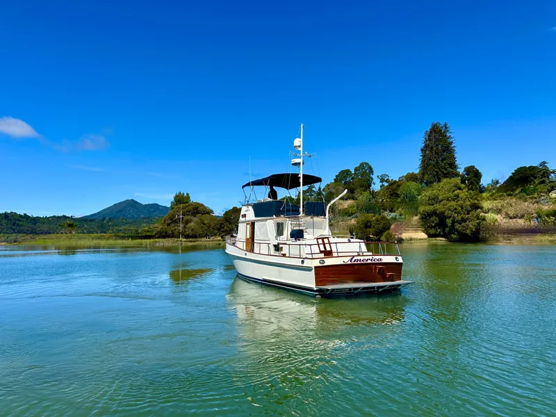 Slide: The Image of 1989 Grand Banks 42 Classic yacht on serene water with lush greenery backdrop. - 7