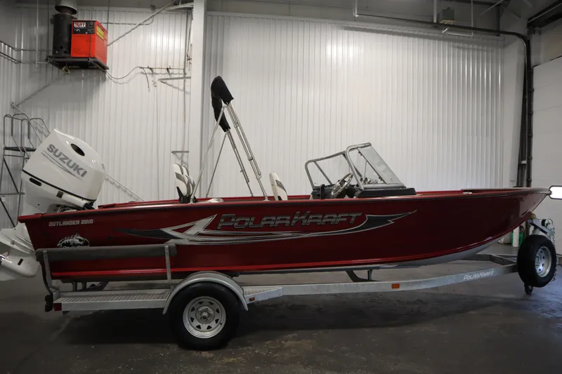 Slide: The Image of Red 2023 Polar Kraft 2010 Outlander DC boat on trailer, indoors, with Suzuki outboard motor. - 4