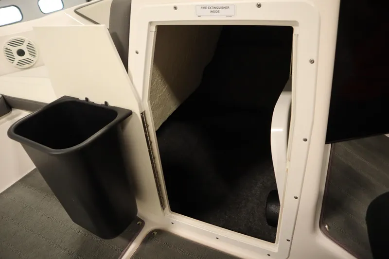 Slide: The Image of 2021 Yamaha Boats 190 AR interior storage compartment with fire extinguisher label and trash bin. - 16